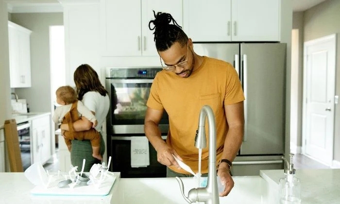 Dad doing the dishes while mom holds baby